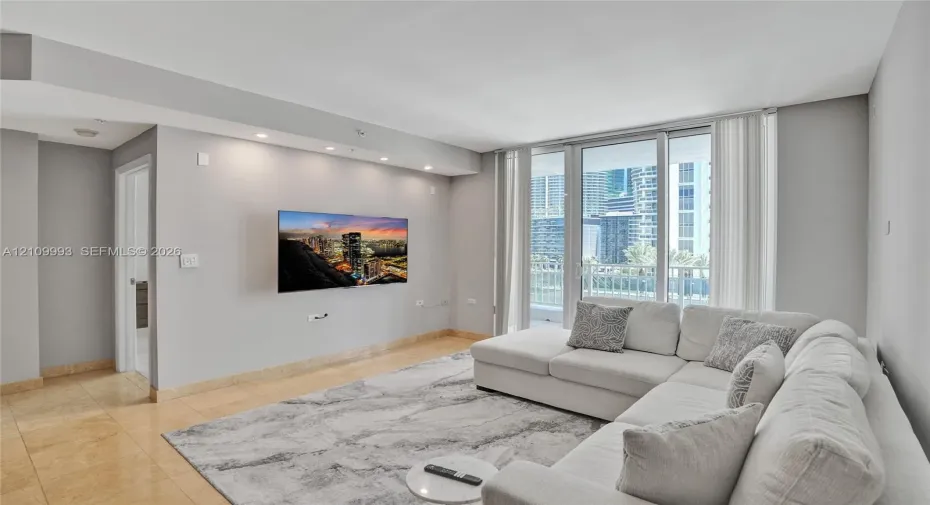 Living area featuring stone-finish flooring, recessed ceiling lighting, a recessed accent wall, and floor-to-ceiling glass sliding doors opening to a balcony