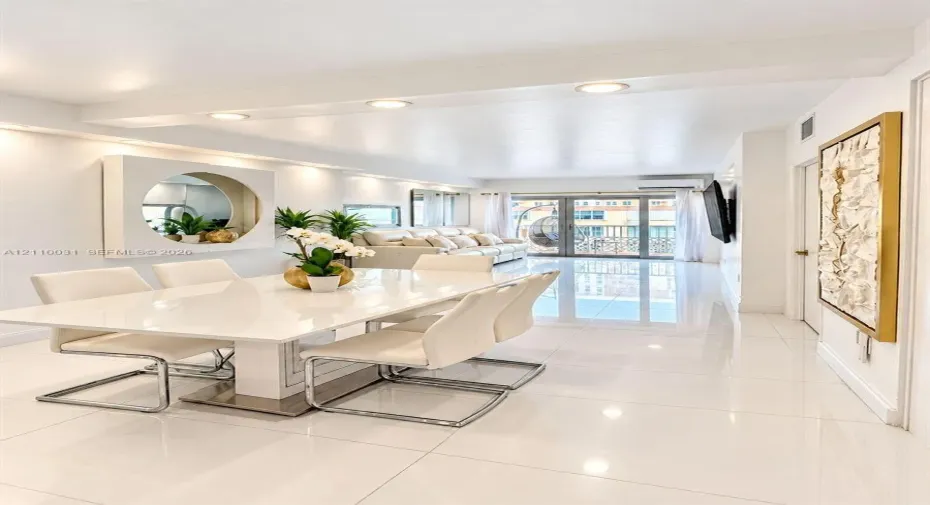 Large-format porcelain tile flooring, recessed ceiling lighting, circular wall-mounted accent mirror, and glass-paned sliding doors opening to a balcony