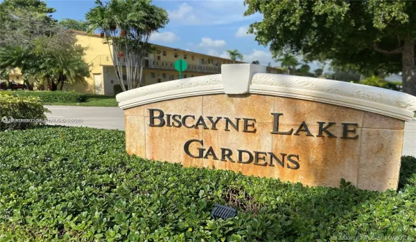 Stone-clad community monument sign featuring dimensional metal lettering and manicured landscape hedging