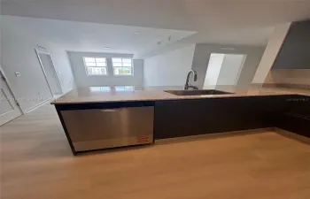 Kitchen featuring a stone-composite countertop, stainless steel dishwasher, undermount stainless steel sink with a high-arch faucet, flat-panel dark cabinetry, and light-toned wood-finish flooring