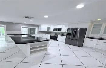 Kitchen featuring white cabinetry, an island with stone-finish countertop, stainless steel appliances, glass-front upper cabinets, and tile flooring