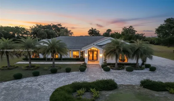Single-story residence with a concrete tile roof, double-door entryway, and paver driveway, set on a landscaped lot with mature palm trees