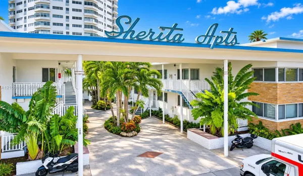 Mid-century architecture featuring a prominent roofline marquee, multi-story white exterior cladding with brick masonry accents, decorative railings, and manicured tropical landscaping