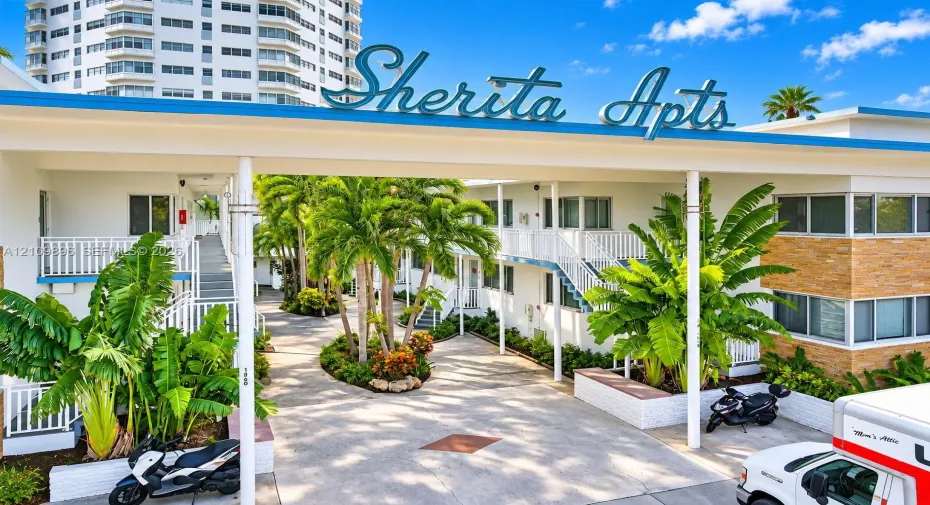 Mid-century architecture featuring a prominent roofline marquee, multi-story white exterior cladding with brick masonry accents, decorative railings, and manicured tropical landscaping