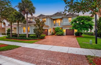 Two-story residence featuring a tile roof, stucco exterior, paver driveway, attached two-car garage, and second-story balcony with decorative metal railing