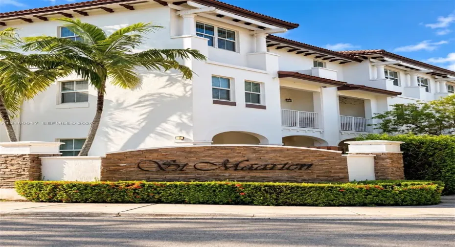 Stucco exterior featuring arched architectural detailing, private balconies with white railings, stone veneer signage, and mature palm landscaping