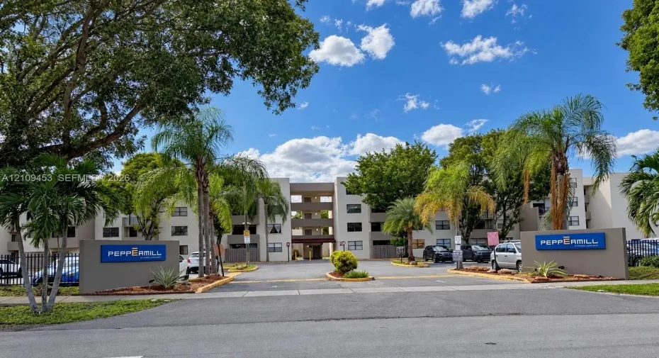 Multi-story residential complex featuring concrete facade, mature palm trees, asphalt paved drive, and prominent signage