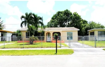 Single-story residence featuring an arched entryway, concrete driveway, and chain-link perimeter fencing
