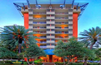 Mid-rise building exterior featuring a structural roof pergola, private balconies on multiple levels, and extensive tropical landscaping