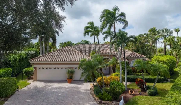 Single-story residence featuring a tile roof, paver driveway, multi-car garage, and mature landscaping