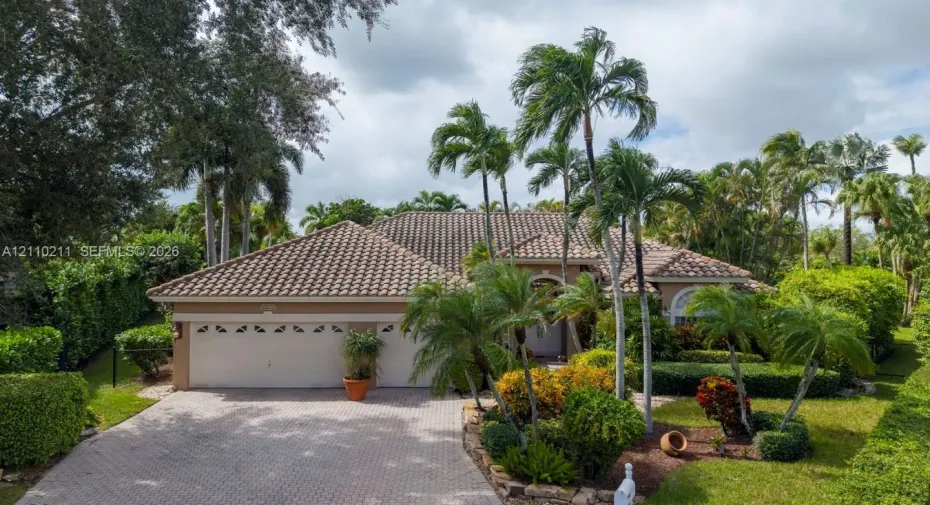 Single-story residence featuring a tile roof, paver driveway, multi-car garage, and mature landscaping