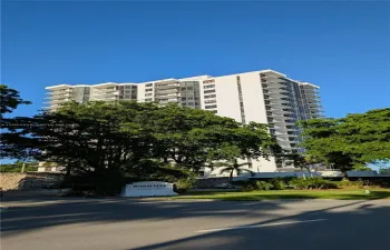 High-rise residential building featuring stacked private balconies, floor-to-ceiling glass windows, and mature exterior landscaping