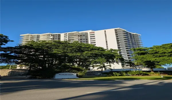 High-rise residential building featuring stacked private balconies, floor-to-ceiling glass windows, and mature exterior landscaping