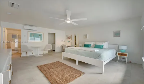 Large-format light-toned tile flooring, white ceiling fan with integrated lighting, wall-mounted ductless air conditioning unit, and neutral interior paint palette