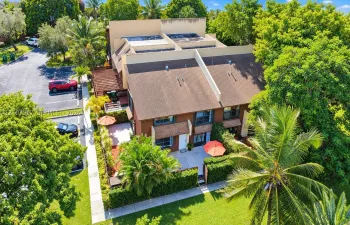 Multi-level exterior featuring a shingled roof, attached wooden pergola, paved ground-level patio, and dense perimeter landscaping
