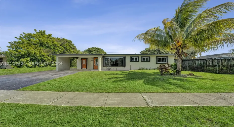Single-story exterior featuring a stucco facade, attached carport, asphalt driveway, and mature landscaping