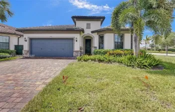 Stucco exterior residence featuring a tile roof, paver driveway, two-car garage, and stone veneer accents