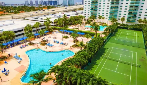 Resort-style amenities featuring dual outdoor swimming pools, two hard-surface tennis courts, and landscaped grounds with mature palm trees