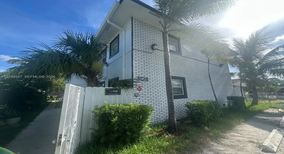 Two-story exterior featuring white brick masonry, dark-trimmed rectangular windows, and a white privacy fence with a gated entrance