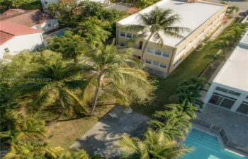 Multi-level exterior featuring a light-toned facade, flat roofline, manicured lawn, established palm trees, and a concrete patio area