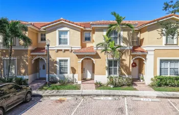 Two-story townhouse exterior featuring a stucco facade, clay tile roof, arched entryway details, and paver walkways