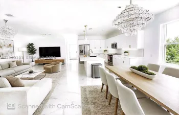 Open-concept living space featuring high-gloss large-format floor tile, white cabinetry with integrated under-cabinet lighting, a central kitchen island with a quartz countertop, and oversized crystal-style chandelier lighting fixtures