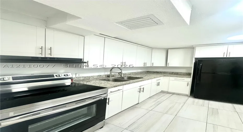 Kitchen featuring white shaker-style cabinetry, stone-finish countertops, dual-basin stainless steel sink with high-arch faucet, and large-format tile flooring