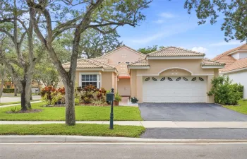 Stucco exterior featuring a tile roof, arched entryway detail, double-car garage, and mature landscape