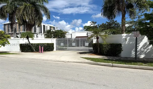 Secure gated entrance featuring metal perimeter fencing, privacy walls, concrete driveway, and mature palm landscaping