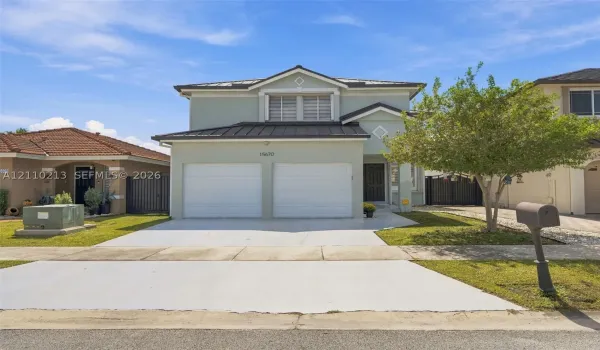 Two-story residence featuring a light-toned stucco exterior, a metal roof, an attached two-car garage, and a paved driveway