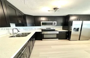 Kitchen featuring dark cabinetry, stone-finish countertops, stainless steel appliances, a double-basin undermount sink with a gooseneck faucet, and wood-finish flooring