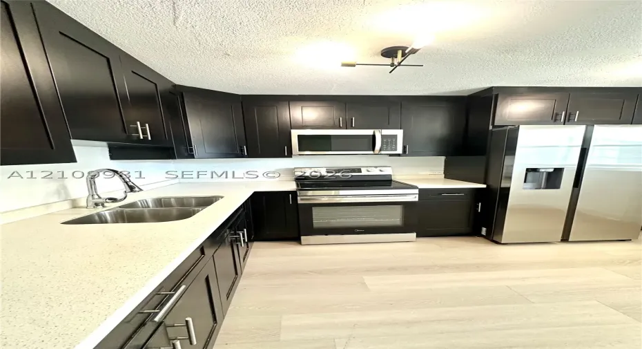 Kitchen featuring dark cabinetry, stone-finish countertops, stainless steel appliances, a double-basin undermount sink with a gooseneck faucet, and wood-finish flooring