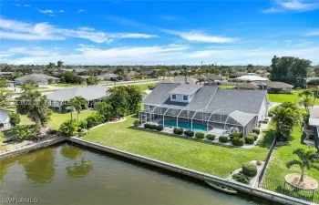 Waterfront property featuring a screened-in lanai with a swimming pool, concrete seawall, and landscaped lawn