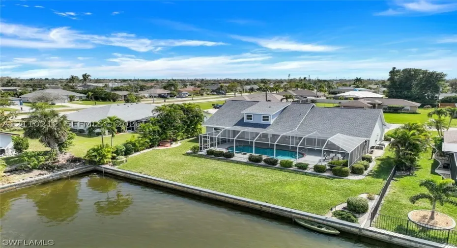 Waterfront property featuring a screened-in lanai with a swimming pool, concrete seawall, and landscaped lawn