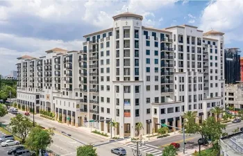 Mid-rise building featuring a light-colored stucco exterior, decorative corner turrets, tiered balconies with wrought-iron railings, and ground-level retail awnings