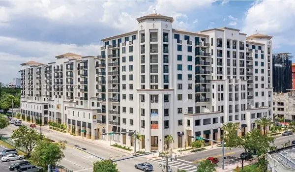 Mid-rise building featuring a light-colored stucco exterior, decorative corner turrets, tiered balconies with wrought-iron railings, and ground-level retail awnings