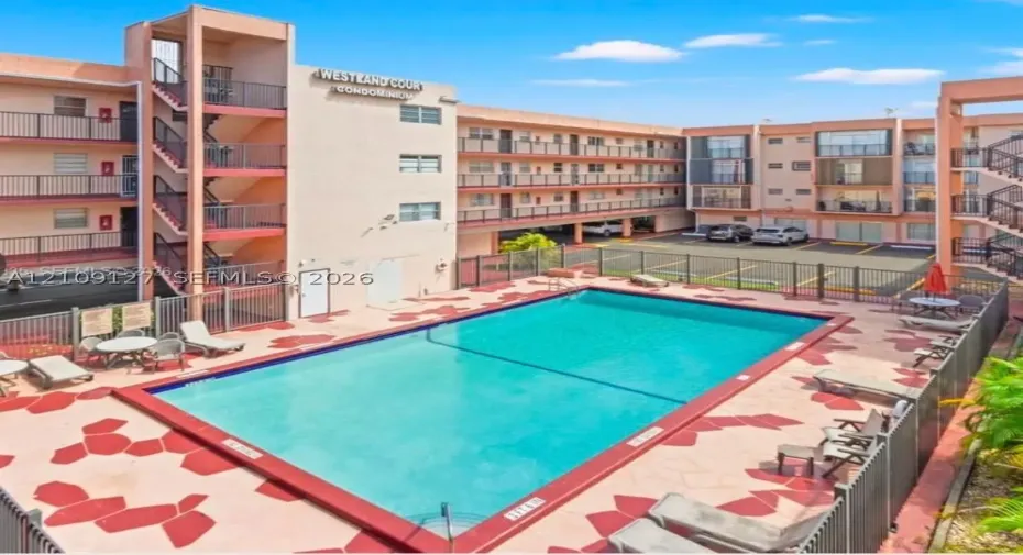 In-ground swimming pool with stone-patterned decking, enclosed by metal fencing