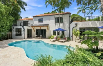 Stucco exterior featuring a clay tile roof, free-form pool, stone-paver pool deck, multiple second-story balconies with iron railings, and dark-frame multi-panel glass doors