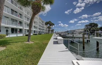 Waterfront property featuring a private boat dock, manicured green space, palm trees, and multi-level exterior balconies