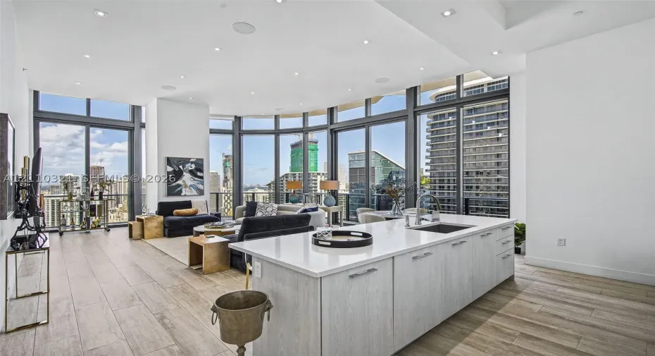 Open-concept kitchen featuring a center island with light-toned cabinetry and a stone-look countertop, floor-to-ceiling windows, wood-finish flooring, and recessed ceiling lighting