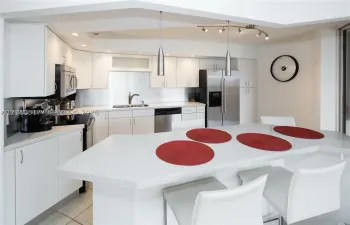 Kitchen featuring flat-panel white cabinetry, solid-surface countertops with an integrated breakfast bar, stainless steel appliances, and dual pendant lighting