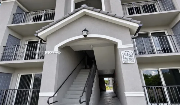 Stucco exterior featuring a pitched tile roof gable, arched entryway, private metal balconies, and concrete stairs with metal railings