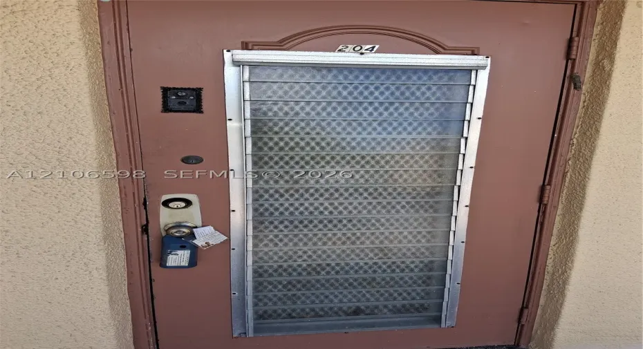 Entry door featuring a textured finish, integrated louvered glass window panel with security grille, and a built-in electronic doorbell system