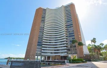 High-rise architectural structure featuring a curved brick and concrete facade with integrated private balconies and floor-to-ceiling glass paneling, situated on a waterfront lot with an attached boat slip