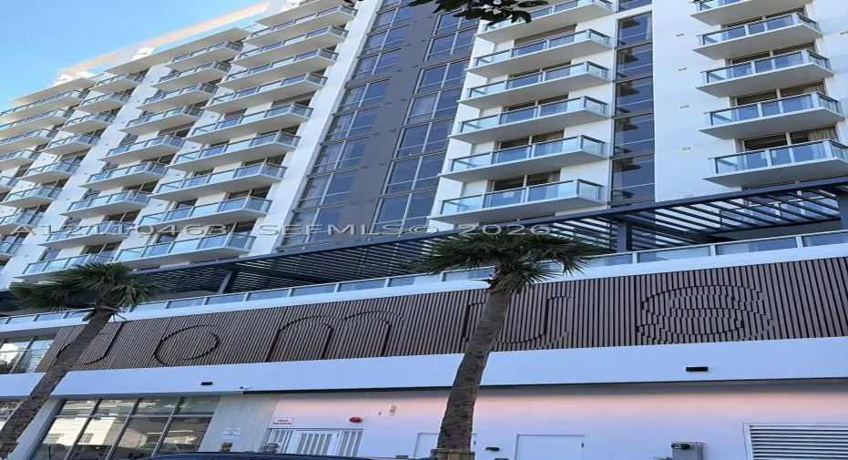 Multi-story modern building facade featuring glass balcony railings, vertical wood-slat accent paneling, and a structural metal pergola