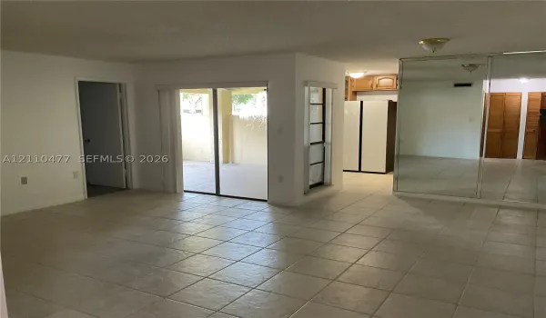 Living area with ceramic tile flooring throughout, sliding glass doors, built-in mirrored closet doors, and wood-finish cabinetry