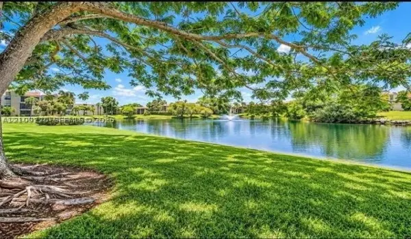 Expansive waterfront grounds featuring a manicured lawn, mature trees, and a central water fountain