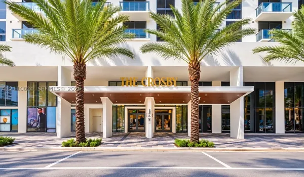 Contemporary building exterior featuring a covered entryway with wood-tone ceiling panels, glass-paneled double doors, floor-to-ceiling windows, and integrated balconies with glass railings