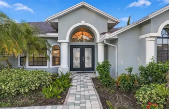 Stucco exterior featuring dual columns, a stone paver walkway, double front entry doors with decorative glass inserts, and a prominent arched transom window