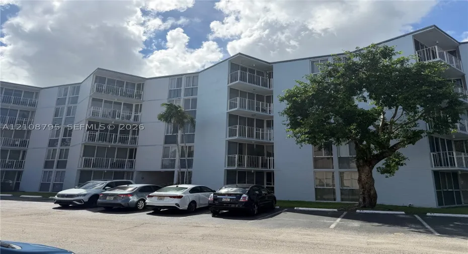 Multi-story structure featuring a light-toned exterior, stacked screened balconies, floor-to-ceiling windows, and dedicated asphalt surface parking